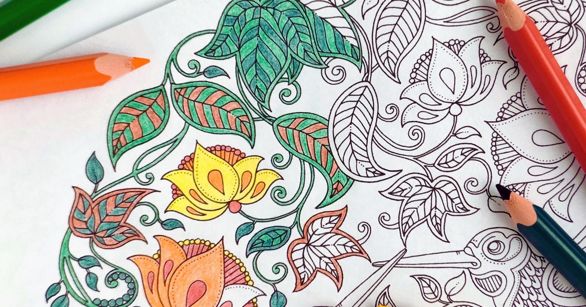 Colouring book page with intricate floral patterns partially filled with bright hues. Pencils in orange, red, and green are scattered around.